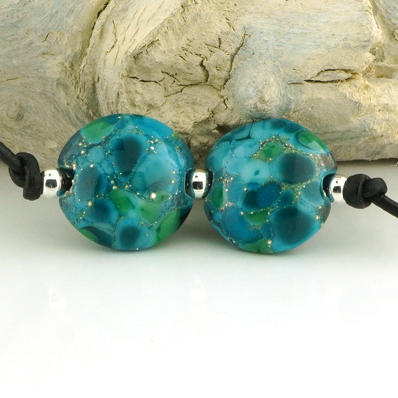 Two round turquoise and teal marbled glass beads on a black cord with silver spacers