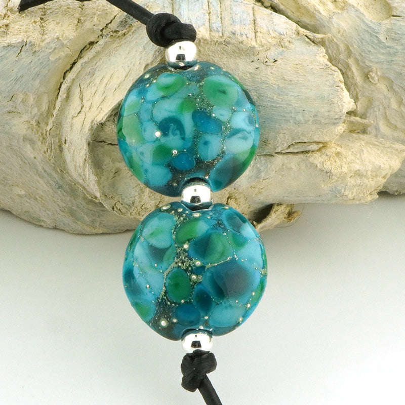 Two round turquoise and teal marbled glass beads on a black cord with silver spacers